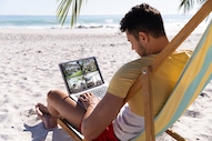 Man sitting on beach watching four security camera views on his laptop.